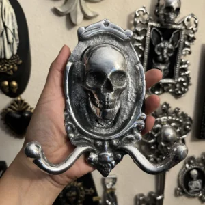 Percha artesanal en metal plateado con calavera, ideal para decoración oscura y exclusiva.