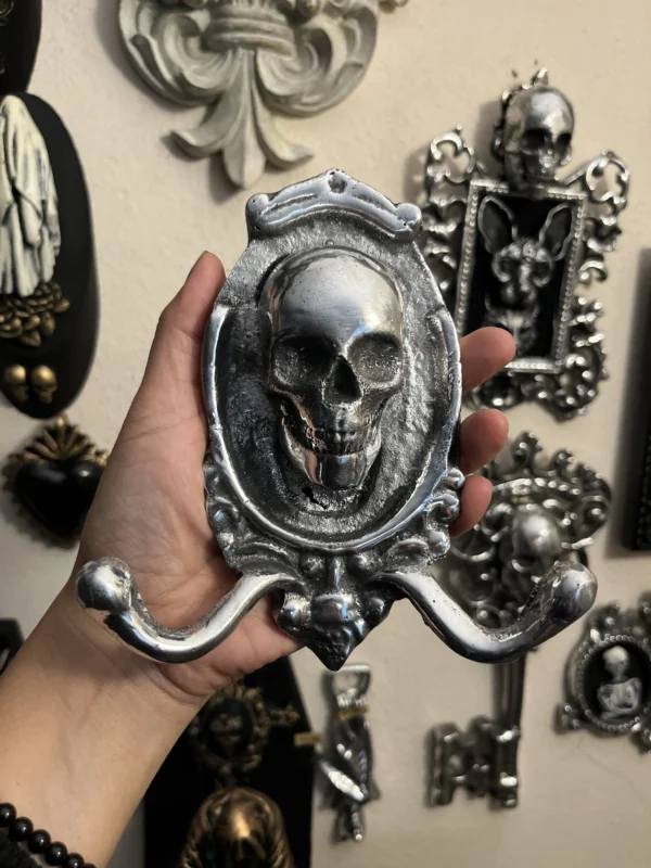 Percha artesanal en metal plateado con calavera, ideal para decoración oscura y exclusiva.